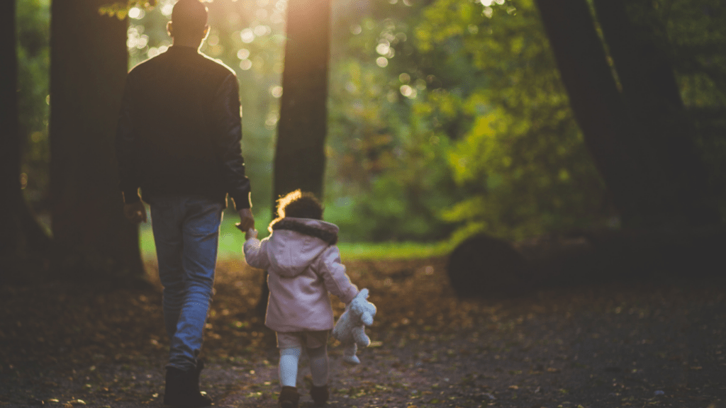 A parent and child walking in the woods at sunset