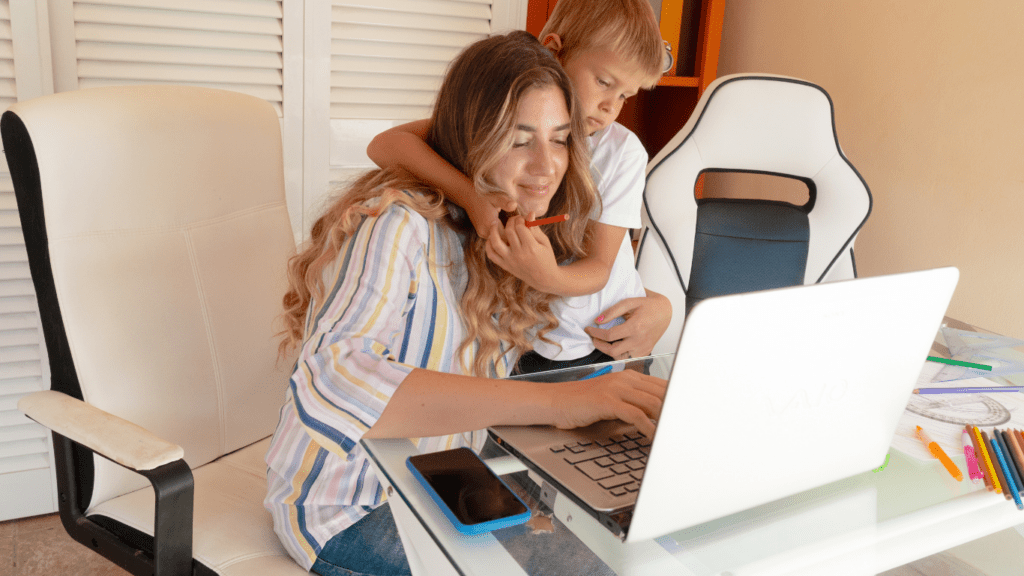 A person and a child sitting at a desk with a laptop.