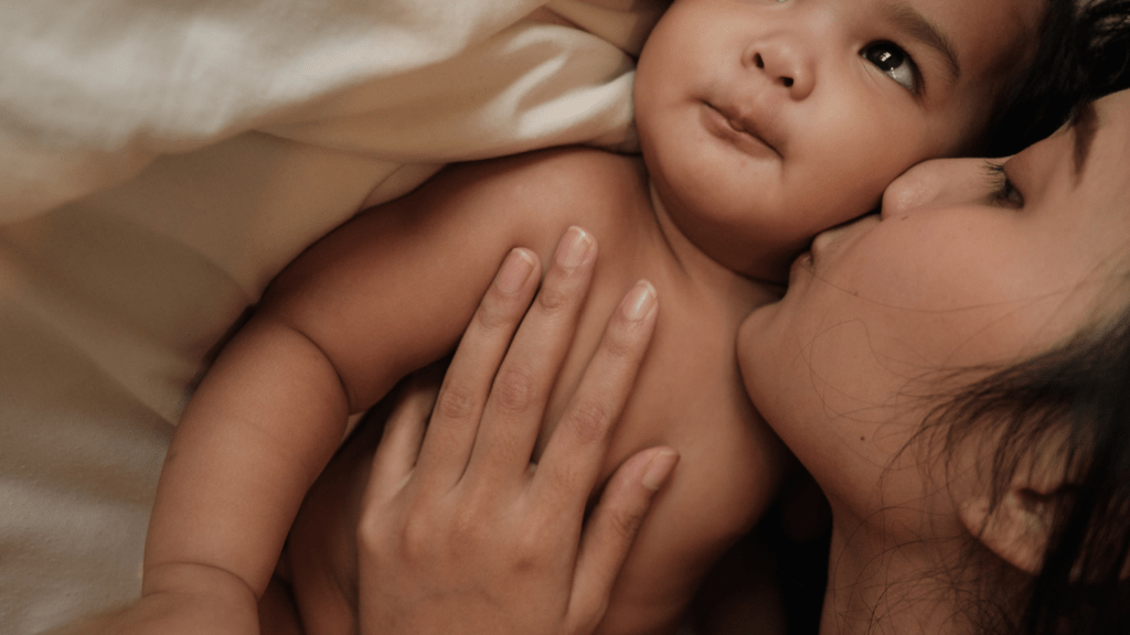 A person kisses their baby on the cheek while laying in bed.