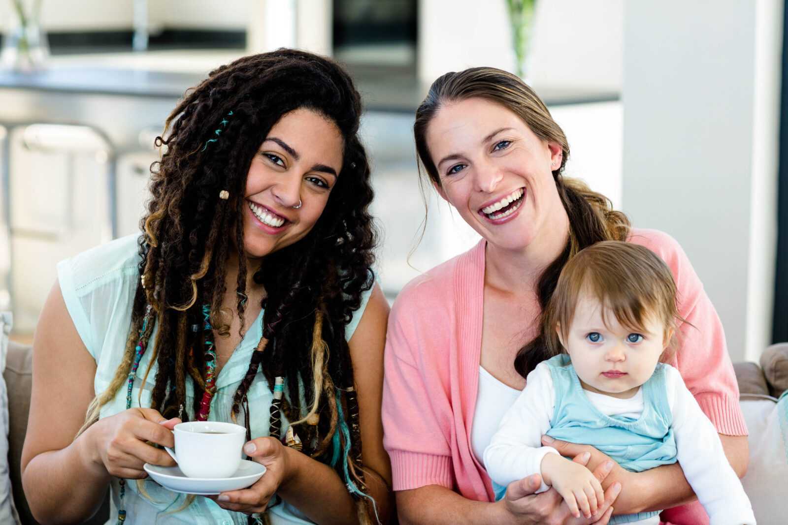 Portrait of two women smiling and sitting on sofa with a baby